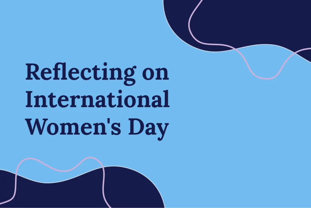 “Reflecting on International Women’s Day,” in the centre on a blue background. Navy blobs at the top and bottom opposite corners with pink outline blobs.